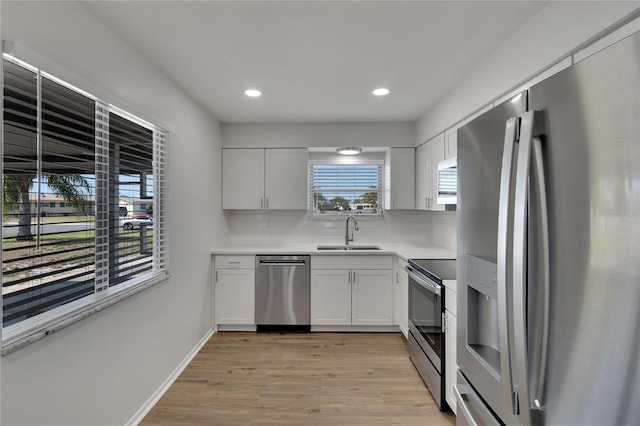 kitchen with tasteful backsplash, sink, white cabinetry, stainless steel appliances, and light hardwood / wood-style flooring