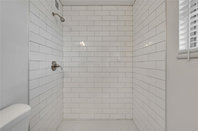 bathroom with a tile shower and toilet