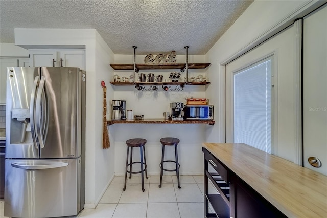 kitchen featuring stainless steel appliances, white cabinets, light tile patterned floors, butcher block countertops, and a textured ceiling