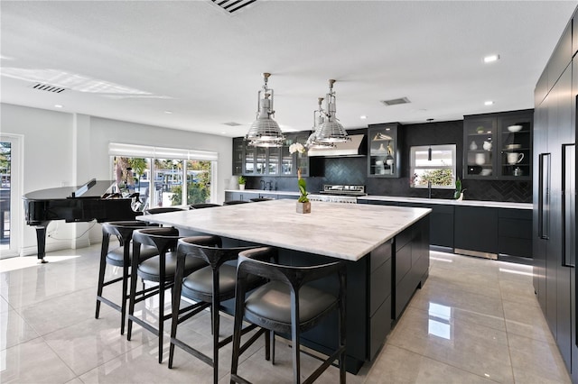 kitchen with a large island, decorative backsplash, hanging light fixtures, stainless steel appliances, and ventilation hood