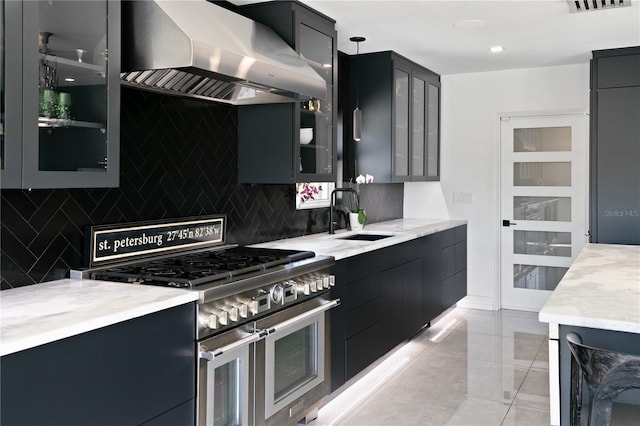 kitchen with tasteful backsplash, light stone countertops, sink, range with two ovens, and wall chimney exhaust hood