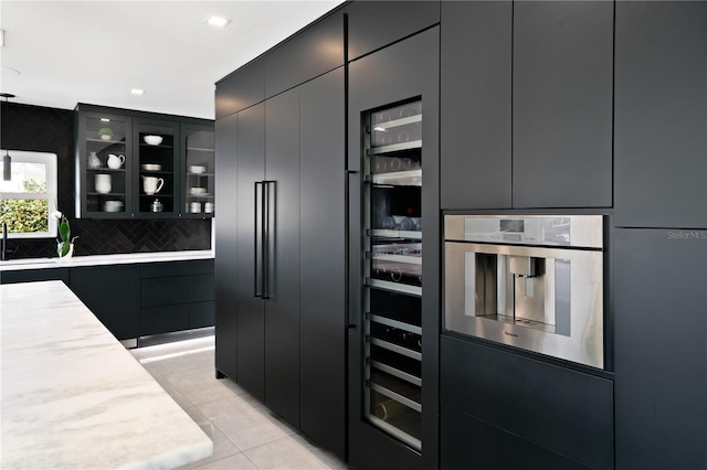 kitchen featuring decorative backsplash, light tile patterned floors, stainless steel oven, pendant lighting, and sink