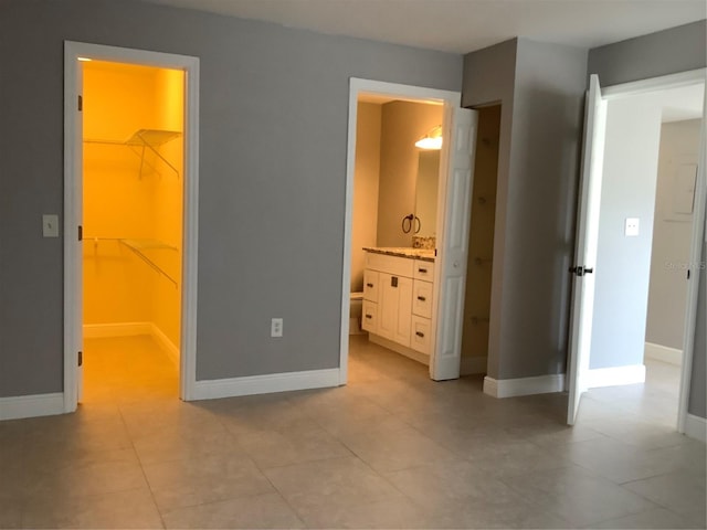 unfurnished bedroom with a closet, a walk in closet, light tile patterned flooring, and ensuite bath