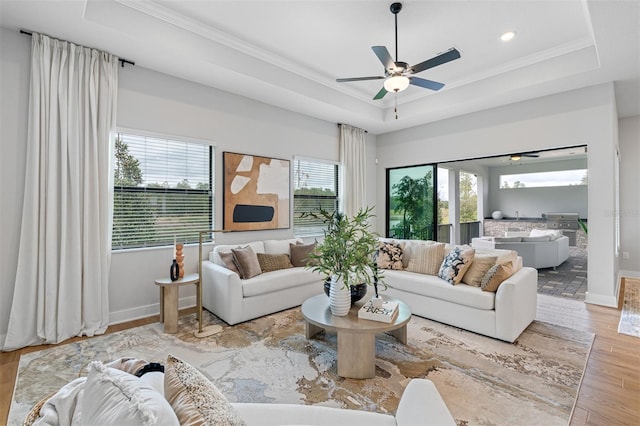 living room with light hardwood / wood-style flooring, ceiling fan, a raised ceiling, and a wealth of natural light