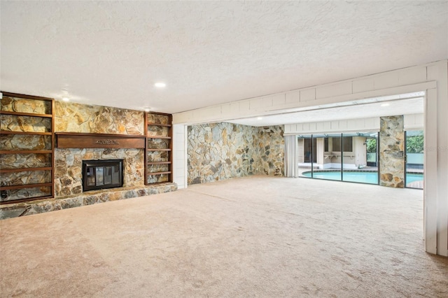 unfurnished living room featuring carpet, a textured ceiling, and a stone fireplace