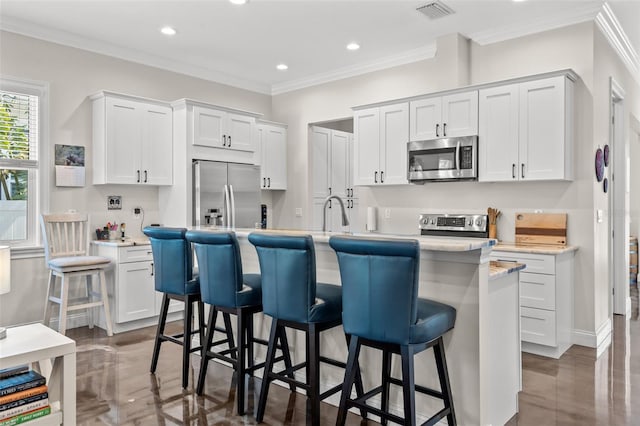 kitchen featuring a kitchen bar, appliances with stainless steel finishes, white cabinetry, and a kitchen island with sink