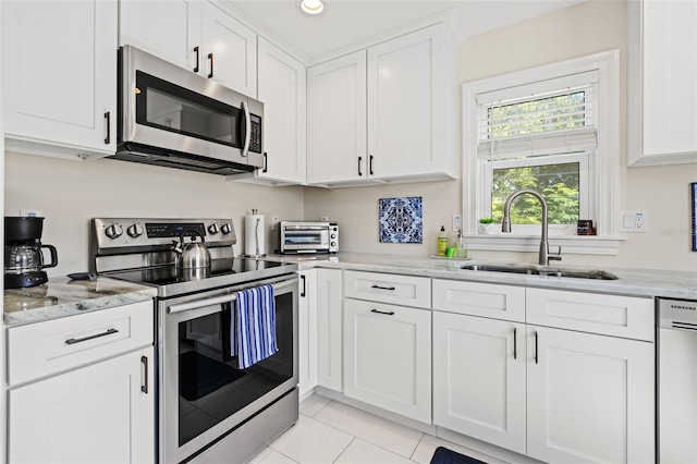 kitchen with light stone counters, stainless steel appliances, sink, white cabinets, and light tile patterned flooring