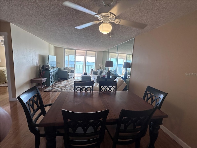 dining space with a wall of windows, a textured ceiling, wood-type flooring, and ceiling fan