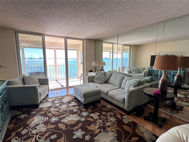 living room featuring floor to ceiling windows, a textured ceiling, a water view, and hardwood / wood-style flooring