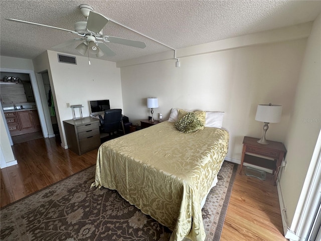 bedroom with hardwood / wood-style floors, ensuite bathroom, a textured ceiling, and ceiling fan