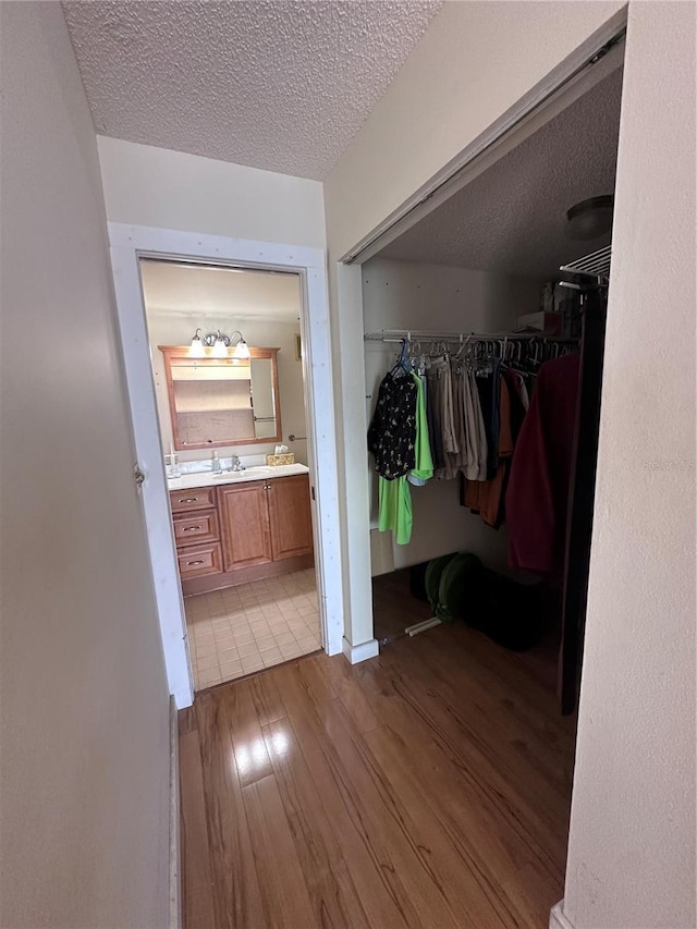 bathroom with wood finished floors, vanity, a textured ceiling, and a walk in closet