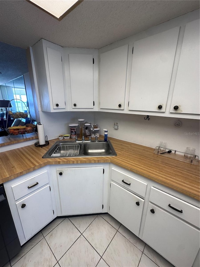 kitchen with black dishwasher, sink, a textured ceiling, white cabinetry, and light tile patterned floors