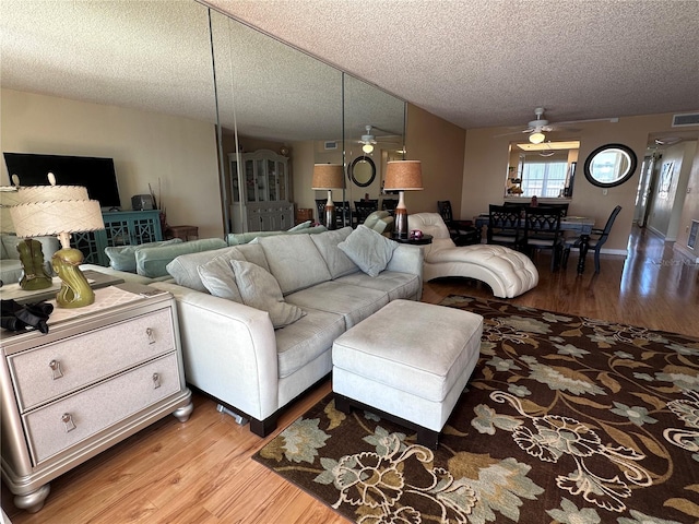 living room with a textured ceiling, wood-type flooring, and ceiling fan