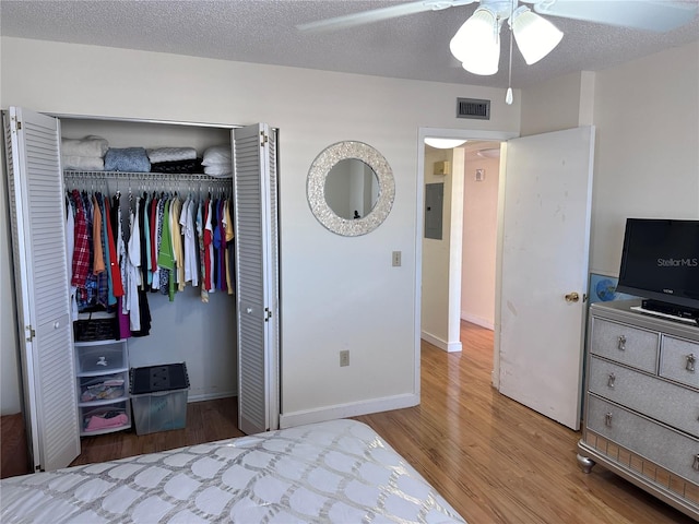 bedroom featuring a closet, hardwood / wood-style floors, electric panel, a textured ceiling, and ceiling fan