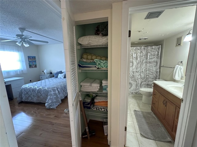 bathroom with wood-type flooring, a textured ceiling, toilet, ceiling fan, and vanity