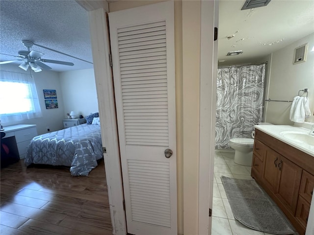 bathroom with a textured ceiling, toilet, ceiling fan, vanity, and tile patterned flooring