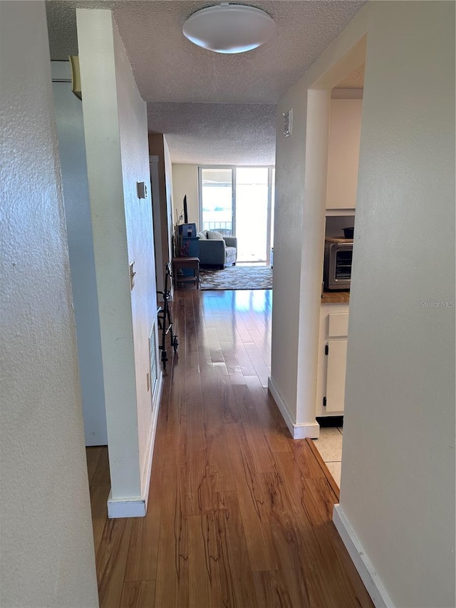 hallway with wood finished floors, baseboards, a textured ceiling, and a textured wall
