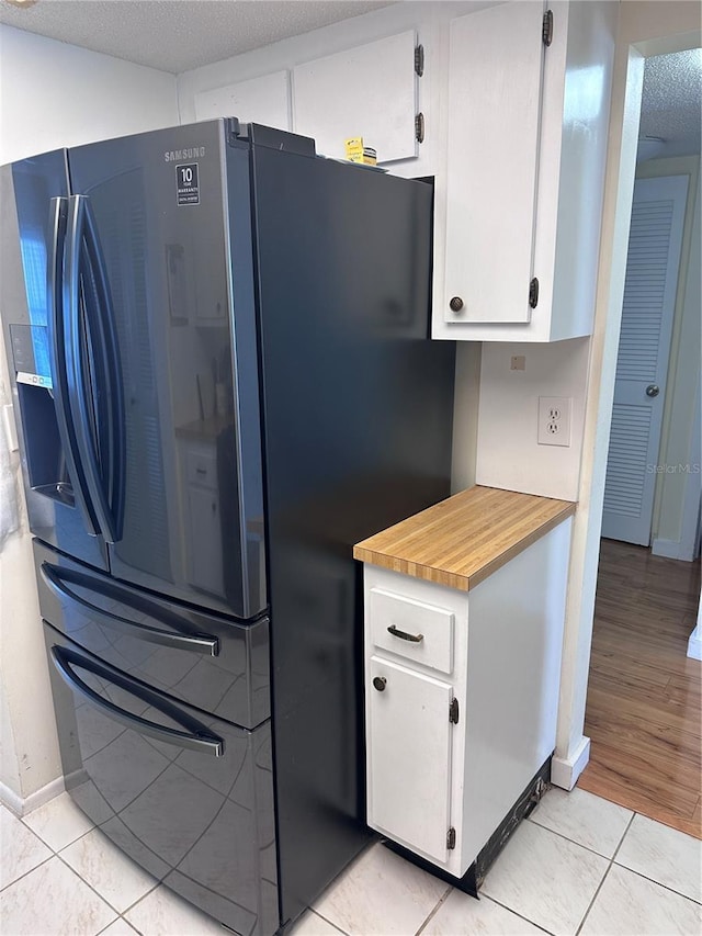 kitchen featuring black fridge, white cabinets, light tile patterned flooring, and baseboards