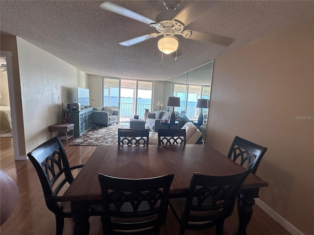 dining room with wood finished floors, a textured ceiling, ceiling fan, expansive windows, and baseboards