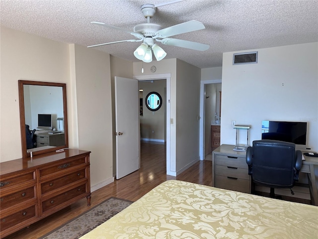 bedroom featuring wood finished floors, an office area, a textured ceiling, a ceiling fan, and baseboards