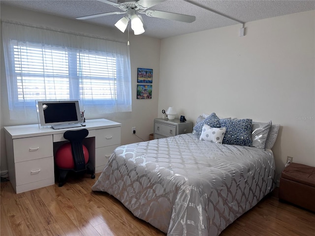 bedroom featuring light wood-style flooring, a textured ceiling, a desk, and ceiling fan
