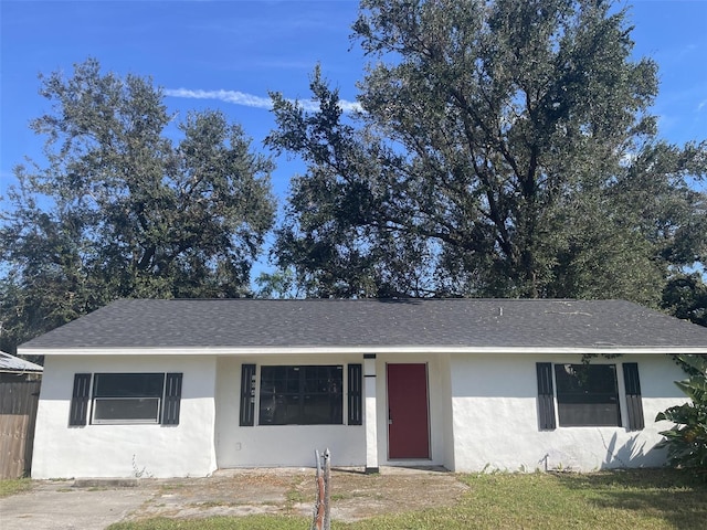 ranch-style home with roof with shingles, stucco siding, and fence