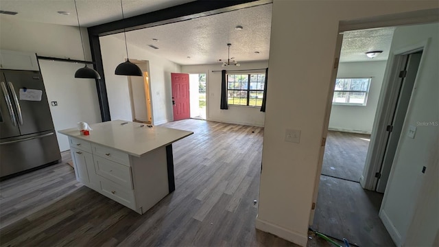 kitchen featuring freestanding refrigerator, white cabinetry, a textured ceiling, and wood finished floors