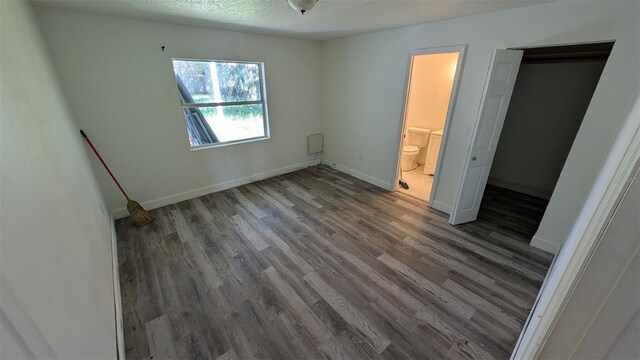 unfurnished bedroom featuring connected bathroom, dark wood-type flooring, and a textured ceiling