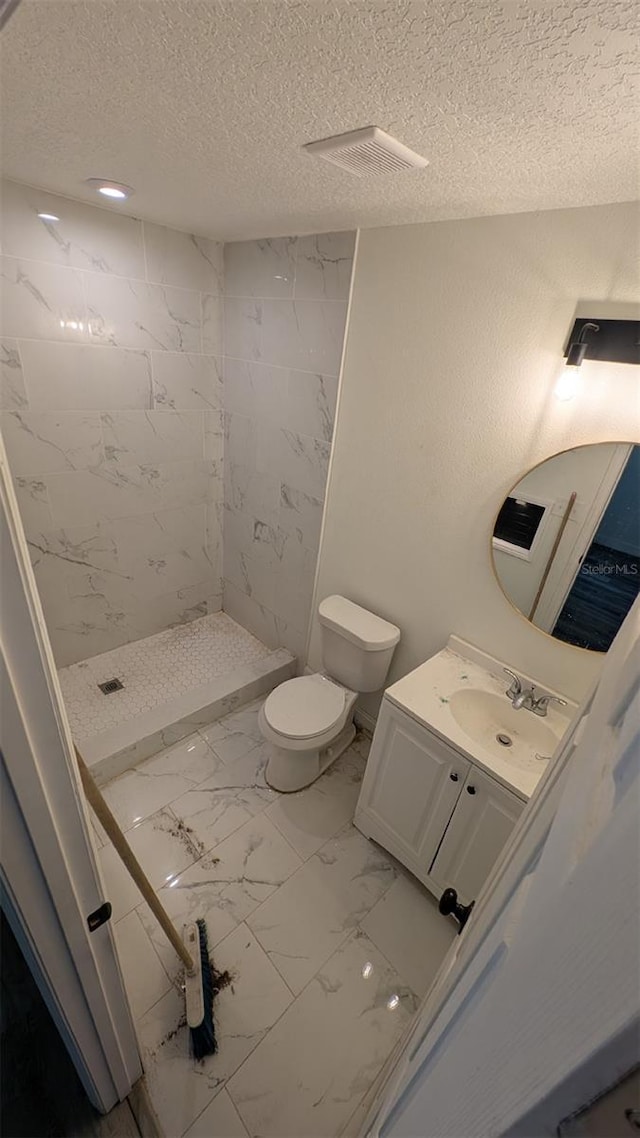 bathroom featuring vanity, toilet, a textured ceiling, marble finish floor, and a stall shower