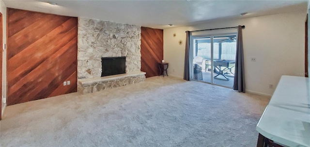 carpeted living room with a stone fireplace and wood walls