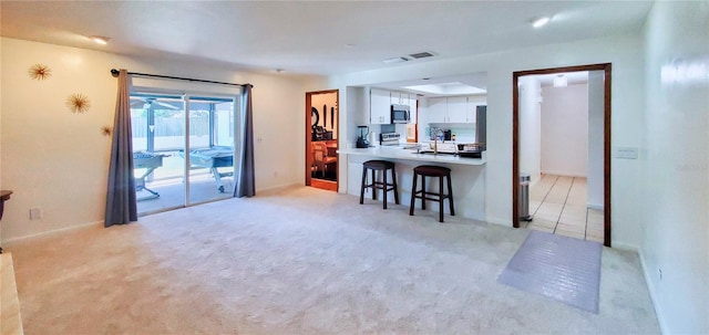 kitchen featuring stainless steel appliances, white cabinets, kitchen peninsula, light carpet, and a kitchen breakfast bar