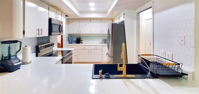 kitchen with stainless steel appliances, white cabinets, a raised ceiling, and backsplash