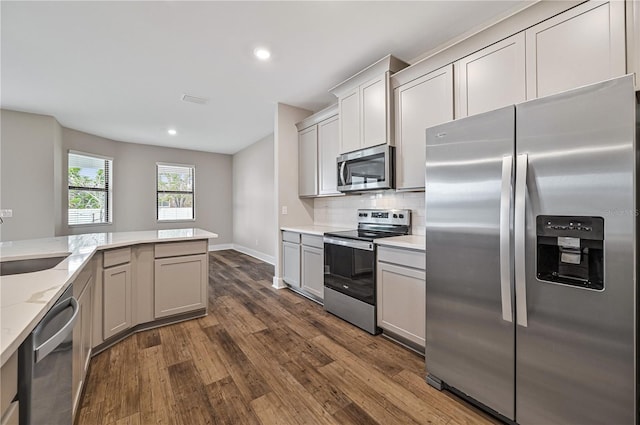 kitchen featuring decorative backsplash, light stone countertops, dark hardwood / wood-style floors, gray cabinetry, and stainless steel appliances