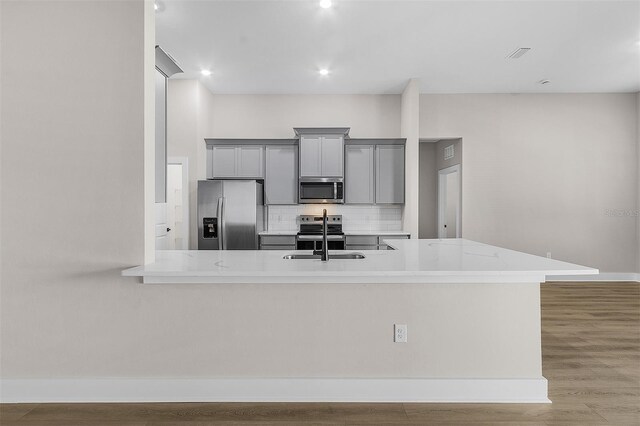 kitchen featuring sink, gray cabinetry, stainless steel appliances, decorative backsplash, and light wood-type flooring