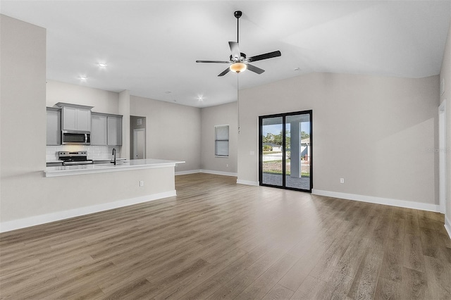 unfurnished living room with vaulted ceiling, ceiling fan, sink, and hardwood / wood-style floors