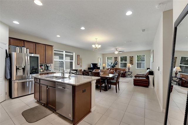 kitchen with light stone countertops, appliances with stainless steel finishes, ceiling fan with notable chandelier, hanging light fixtures, and a kitchen island with sink