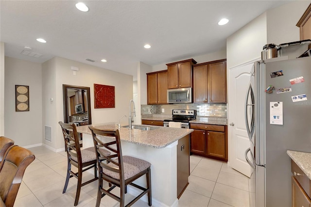 kitchen featuring decorative backsplash, an island with sink, light tile patterned flooring, sink, and stainless steel appliances