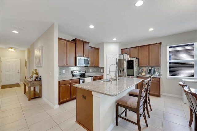 kitchen featuring sink, stainless steel appliances, light stone counters, a breakfast bar area, and a kitchen island with sink