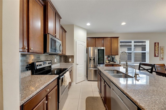 kitchen featuring tasteful backsplash, light stone counters, appliances with stainless steel finishes, light tile patterned flooring, and sink