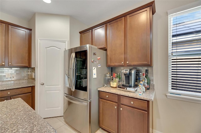 kitchen featuring light stone counters, tasteful backsplash, stainless steel fridge with ice dispenser, and light tile patterned flooring