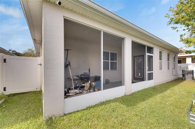 exterior space with central air condition unit, a sunroom, and a lawn