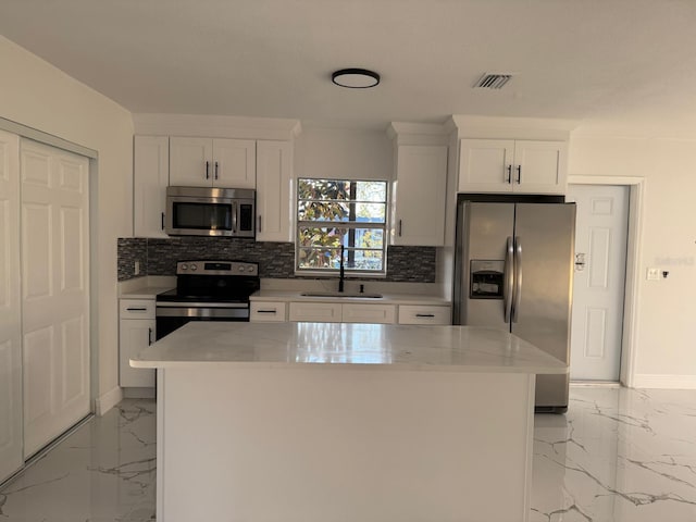 kitchen featuring white cabinets, a kitchen island, light stone counters, and appliances with stainless steel finishes