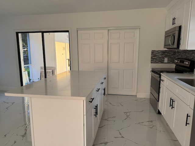 kitchen with white cabinets, appliances with stainless steel finishes, a kitchen island, and light stone countertops