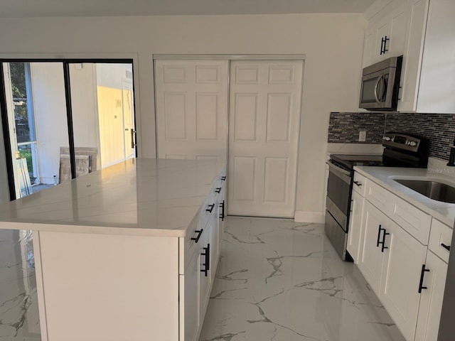 kitchen with sink, stainless steel appliances, a kitchen island, light stone counters, and white cabinets