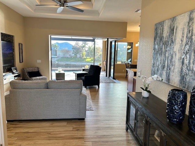 living room featuring ceiling fan, a tray ceiling, and light wood-type flooring