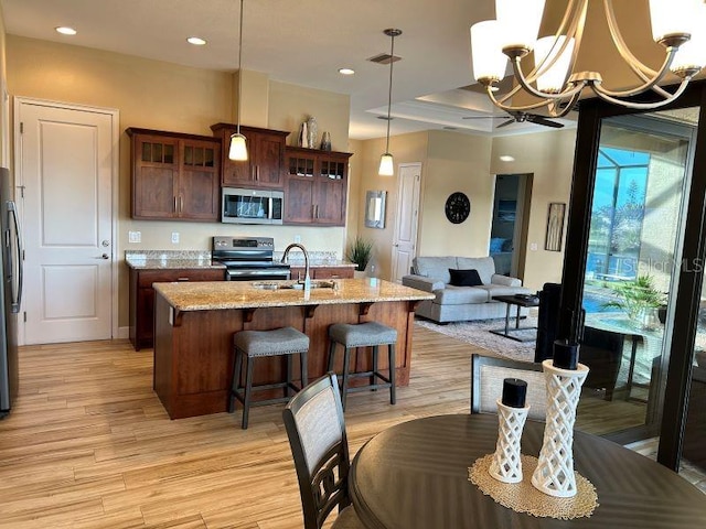 kitchen featuring decorative light fixtures, an inviting chandelier, appliances with stainless steel finishes, light stone counters, and light hardwood / wood-style floors