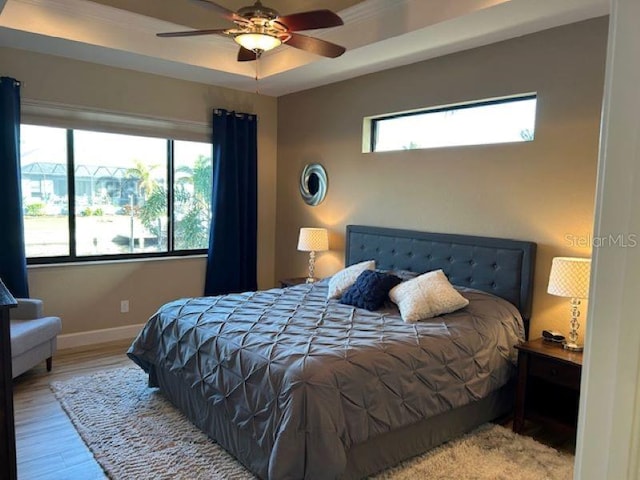 bedroom with light hardwood / wood-style floors, multiple windows, a tray ceiling, and ceiling fan