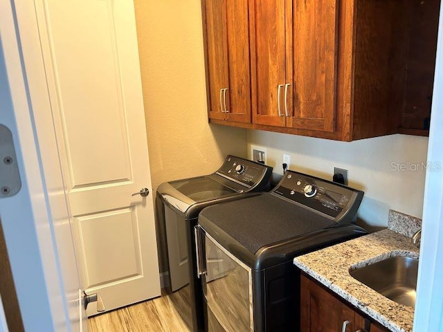 laundry room featuring sink, washer and clothes dryer, light wood-type flooring, and cabinets