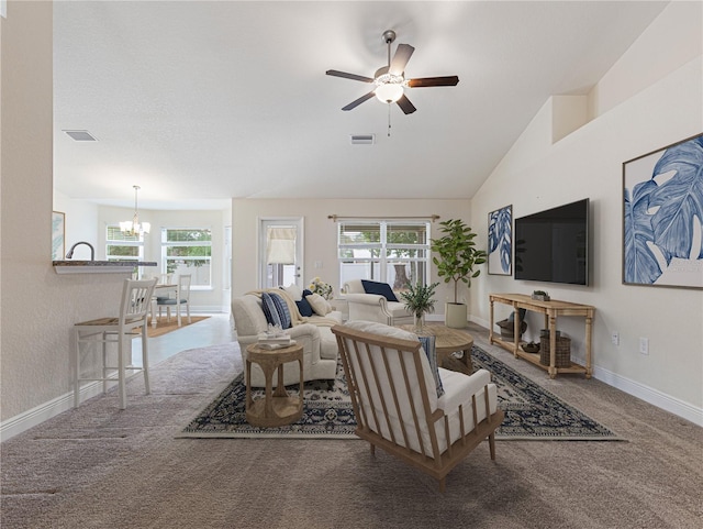 carpeted living room with ceiling fan with notable chandelier, plenty of natural light, and high vaulted ceiling