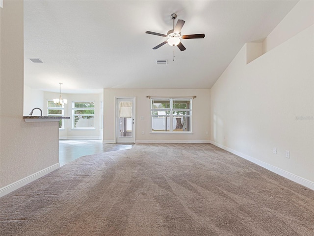 unfurnished living room featuring ceiling fan with notable chandelier, light colored carpet, lofted ceiling, and a healthy amount of sunlight